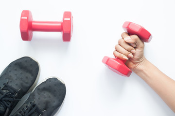 Creative flat lay of woman hand holding red dumbbell with sport items on white background