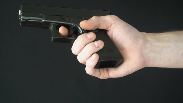 young man inserts the clip into gun black. slow motion.