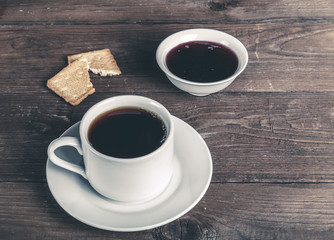 Cup of tea with jam and biscuits on old wooden table against the background of burlap. Toned
