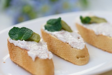 Baguette slices with ham mousse spread, gherkin and mint