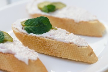 Baguette slices with ham mousse spread, gherkin and mint
