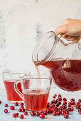 Cranberry drink.  Homemade cranberry drink in a glass jug and in mugs on a light background.