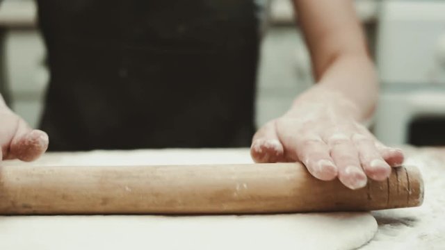 Female baker rolling fresh dough with wooden stick at home. Pizza cooking concept. 