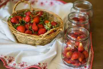 Close-up of strawberries for winter, jar and basket of fresh ripe fruit. Shallow depth of focus. Concept of home coziness.