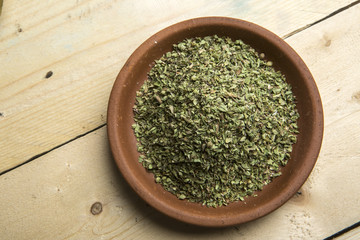 foto ortogonale di una Ciotola in coccio con dentro foglie di origano essiccato, sopra tavolo in legno