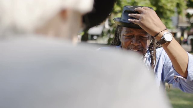 Jamaican man smiles as he plays a game of chess with an old friend in the park