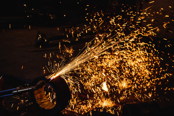 Worker cutting steel plate with acetylene welding cutting torch and bright sparks in steel construction industry.