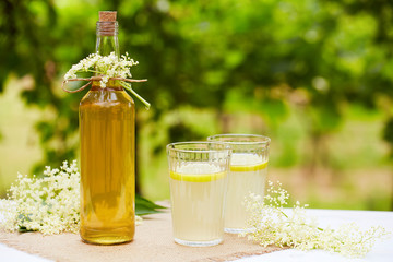 Two glasses of elderflower lemonade and bottle of homemade syrup