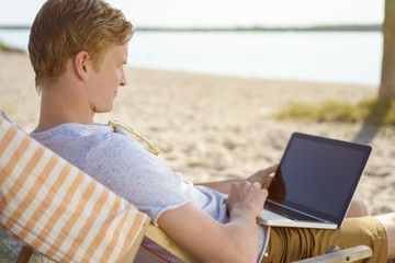 Young man working on his laptop on a beach