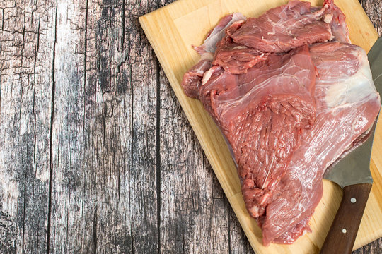   Meat veal.  A raw veal chop and a knife on a kitchen cutting board on a wooden background.
