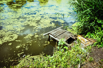 Wooden platform for fishing on the river in summer. Duckweed, reflection of trees and sky in the water.