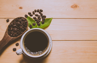 A cup of coffee with coffee beans and leaf over wooden table. Top view. Copy space.