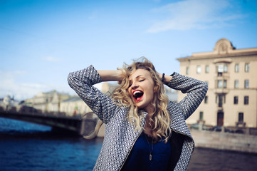 Fototapeta na wymiar close-up portrait of a young girl hipster beautiful blonde with red lips laughing and posing against the backdrop of the city
