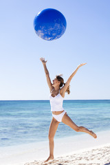 femme riant qui saute avec une balle de gymnastique sur la plage