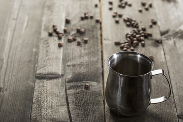 recipiente in metallo per scaldare le bevande e chicchi di caffè sparsi sopra tavolo in legno scuro