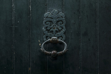 Old dark forest green painted door knocker on old shabby wooden door