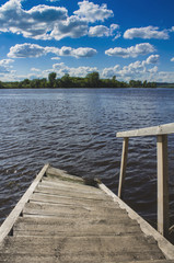 Obraz premium Wooden steps for boarding a boat go into the water under a blue sky with white clouds.
