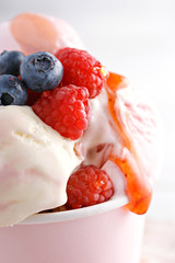 Ice cream close-up. Fresh fruits on ice-cream with red topping. Blueberries and raspberries
