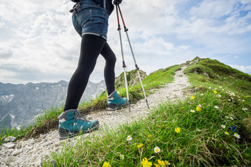 Woman running on narrow mountain trail with hiking poles.