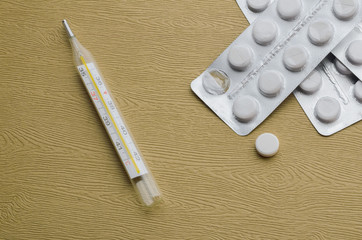 A pack of pills and thermometer on a wooden table