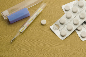 A pack of pills and thermometer on a wooden table