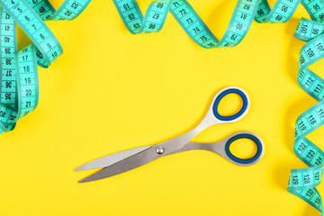Scissors of silver color and curled cyan measuring tape