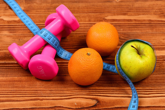 sport object concept, dumbbells with measuring tape, orange and apple