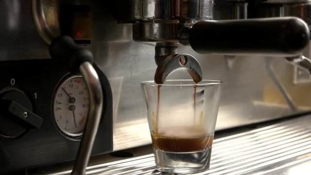 Coffee machine pours espresso. Shot glass close up.