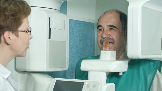 Dentist talking to a senior patient before examination by using panoramic and cephalometric X-Ray scanner