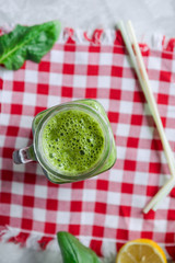 Top view Healthy green spinach smoothie in a jar mug with ingredients on the checkered napkin on the white marble table. Selective focus.