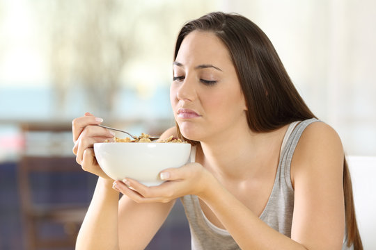 Disgusted woman eating cereals with bad taste