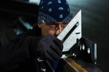Welder checking square on part with safety glasses and bandanna on head
