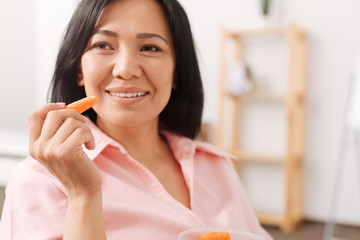 Cheerful asian pregnant woman eating carrot