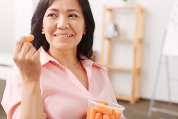 Glad asian woman eating baby carrot