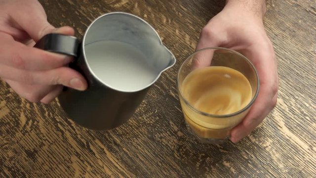 Hands add milk to coffee. Barista holding glass and jug. Tips for new baristas.