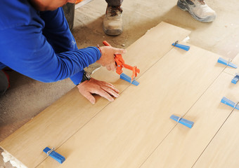 Bricklayer placing a porcelain stoneware floor with special tools, plastic tongs and blue adjustment wedges