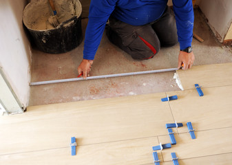 Bricklayer taking measurements with a meter during the placement of a new porcelain stoneware floor in the house living room © joserpizarro