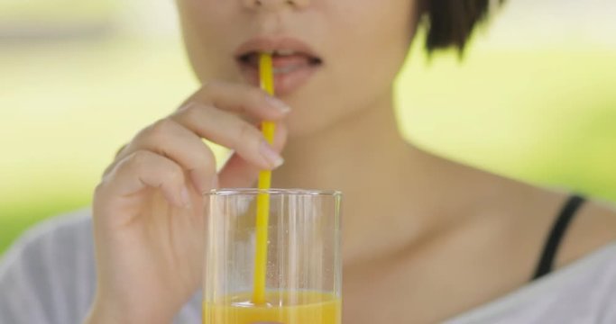 Young woman drinking fresh orange juice outdoors at summer park. Healthy lifestyle food.