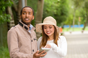 Beautiful young multi-ethnic couple having fun together at the park, man looking somewhere while woman watching his cellphone