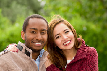 Beautiful and smiling happy interracial young couple looking at camera in park in outdoors