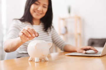 Obraz na płótnie Canvas Positive woman putting coins into piggy bank