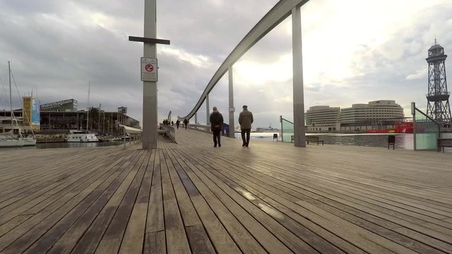 This is footage of an eldery couple walking slowly, enjoying the view on the shore of a big city near the port. Wooden floor and eary sunset.