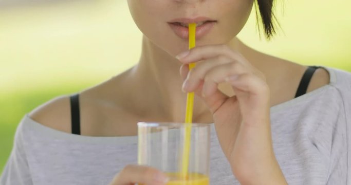 Healthy lifestyle food. Young woman drinking fresh orange juice outdoors at summer park.