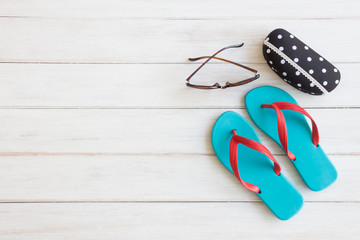 Women's summer accessories items with blue flip flops and sunglasses on white rustic wooden board background with copy space