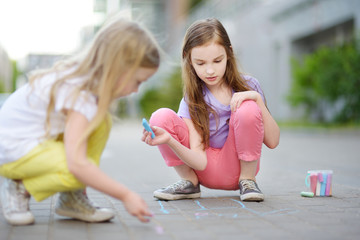Cute little girl drawing with colorful chalks on a sidewalk. Summer activity for small kids. © MNStudio