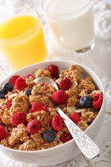 Multigrain granola with dried raspberries, nuts and blueberries, milk and juice close-up. vertical