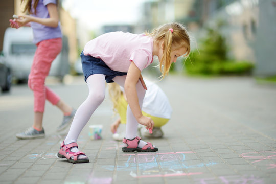 Cute little girl drawing with colorful chalks on a sidewalk. Summer activity for small kids. © MNStudio