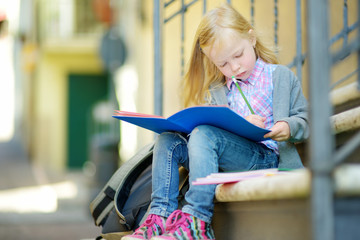 Adorable little schoolgirl studying outdoors on bright autumn day. Young student doing her homework. Education for small kids.