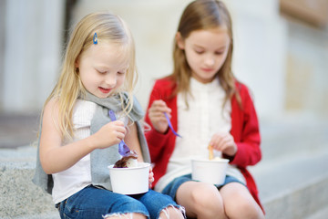 Two cute little sisters eating ice-cream while sitting on the stairs on summer day