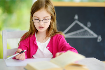 Smart little schoolgirl with pen and books writing a test in a classroom. Child in an elementary...